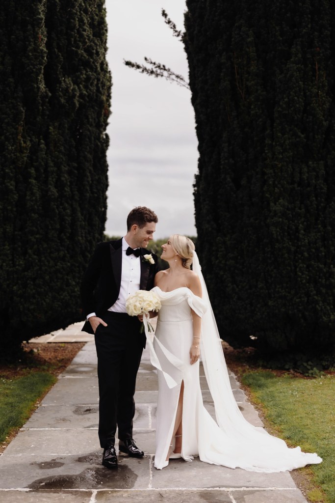 bride and groom embrace look at each other on pathway to garden