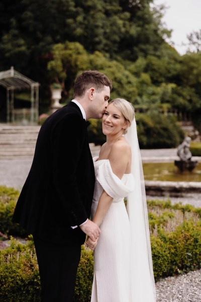 groom goes in to kiss bride on the cheek in garden