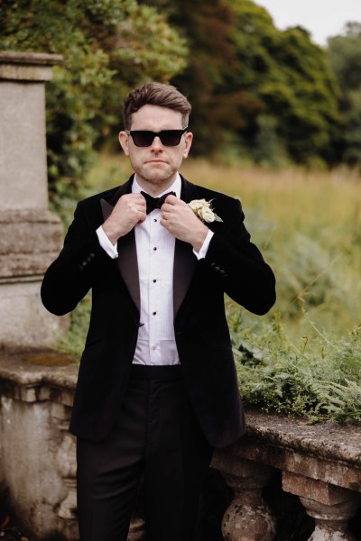 groom wears sunglasses fixing u p his tie