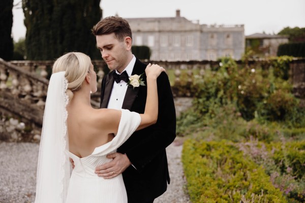 bride has arms on grooms shoulders they face each other in garden