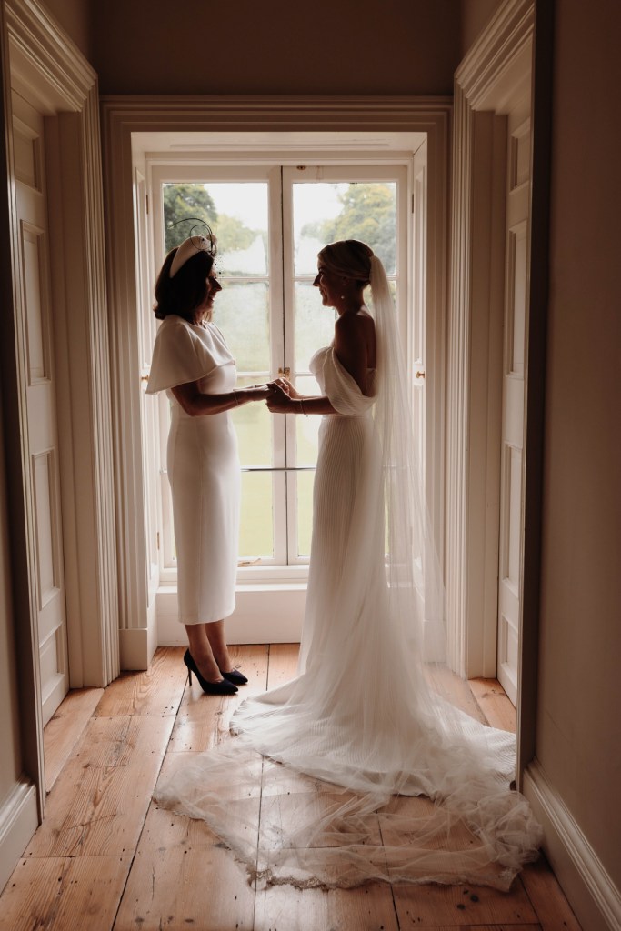 mother and daughter hold hands at window both wear white