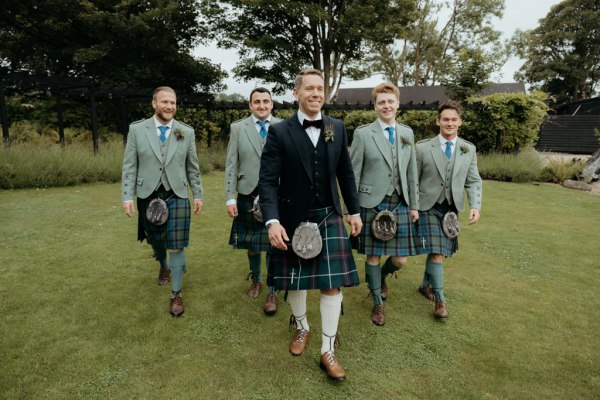 groom and groomsmen walk on the green grass in garden