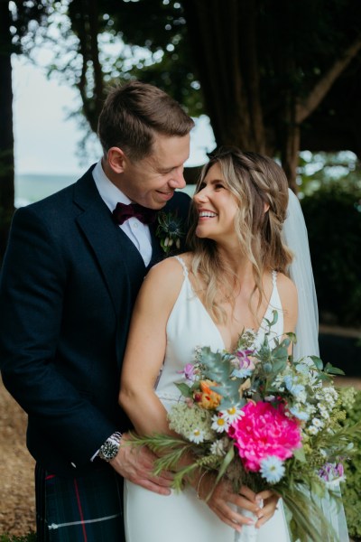 bride looks at groom over the shoulder in garden setting