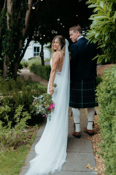 bride and groom walk on pathway to garden looking over their shoulders