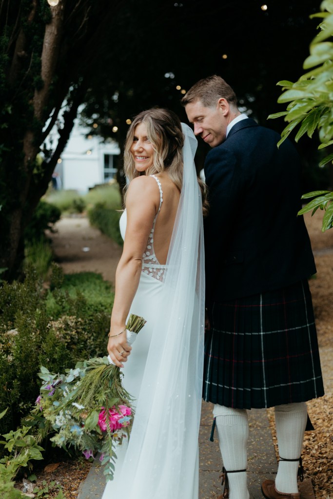 bride and groom walk on pathway to garden looking over their shoulders