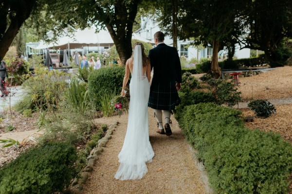 bride and groom walk on pathway to garden walking away from camera