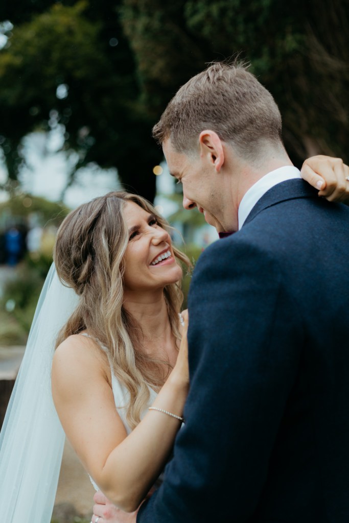 bride and groom hug and embrace in garden facing each other smiling