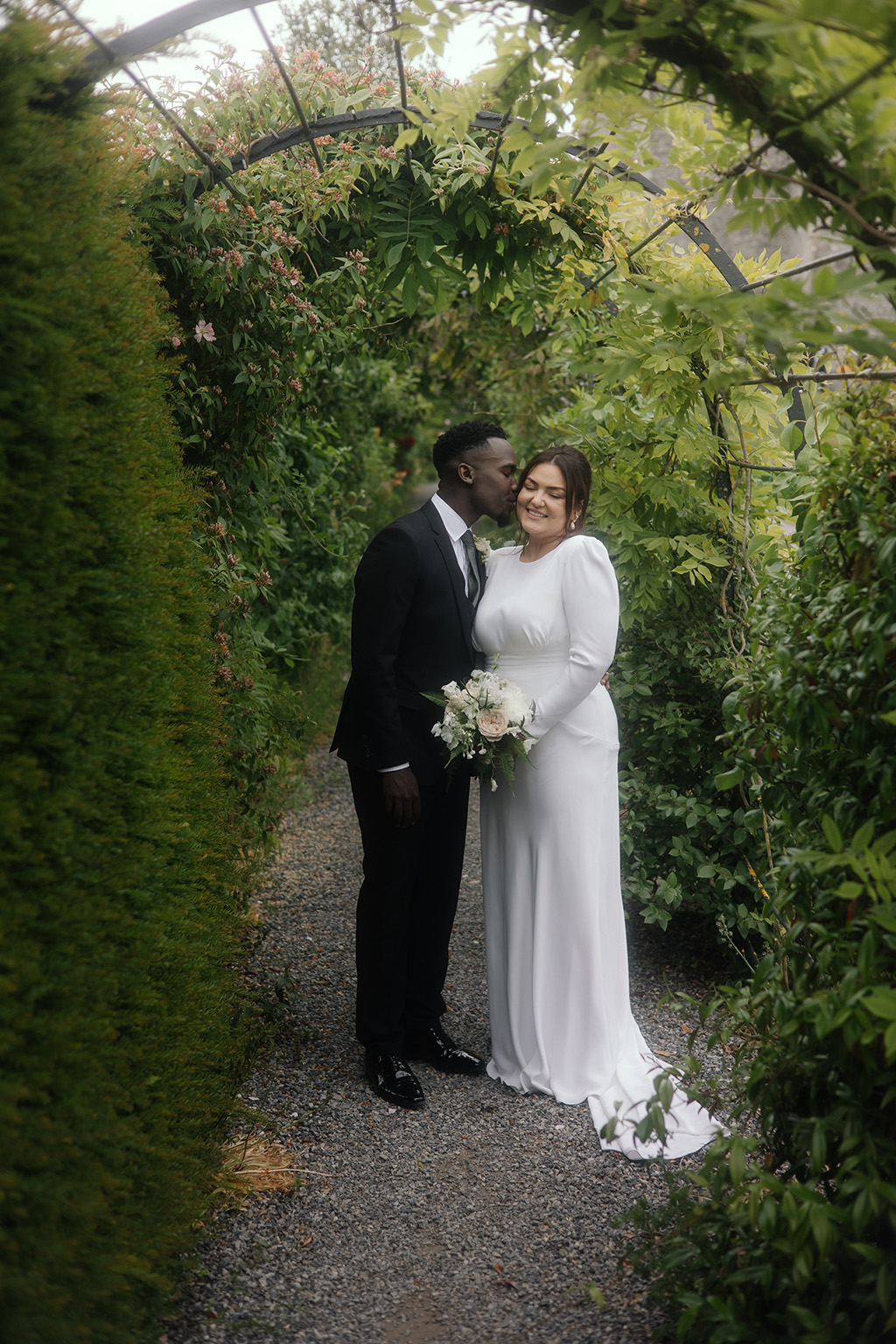 groom kisses bride on the cheek in forest garden setting