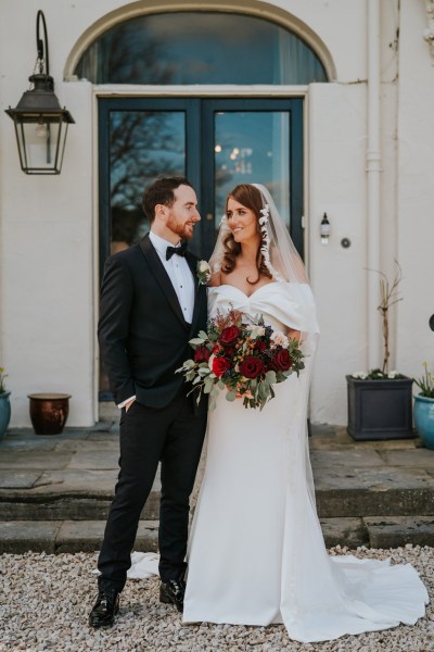 bride and groom pose outside of wedding venue entrance she holds her bouquet