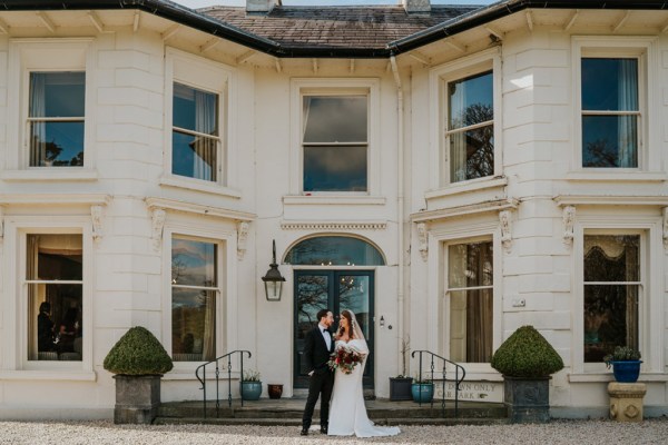 bride and groom pose outside of wedding venue entrance