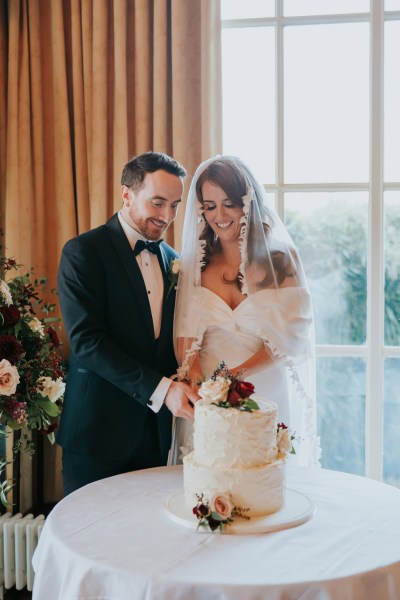 bride and groom cut the white creamy cake that has flowers on top