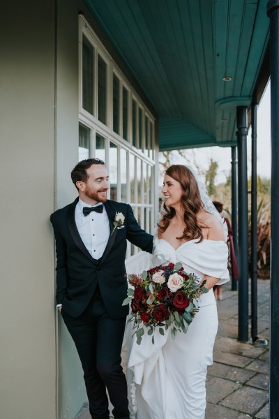 bride and groom stand together against wall she holds bouquet