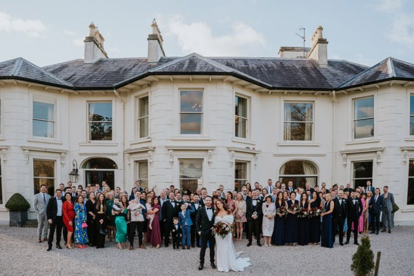 bride groom and guests in background stand in the courtyard to wedding venue