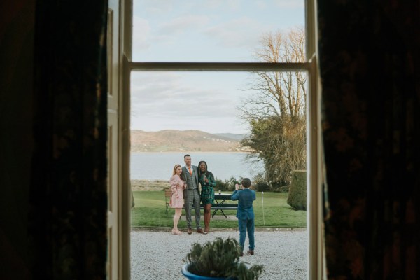 man takes photo of three friends outside lake landscape