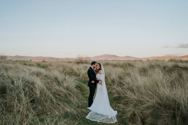 bride and groom walk through the sand and grass landscape they hug