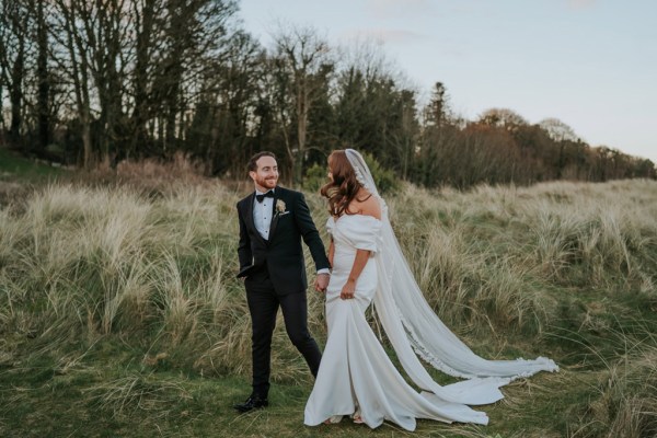 bride and groom walk through forest veil follows trees dark