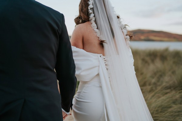 bride and groom embrace and hug on the beach and sand they walk away back of brides bridal gown dress