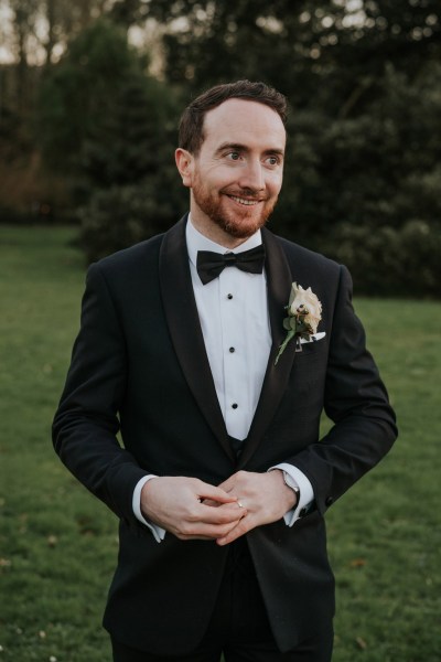 groom stands and smiles on grass