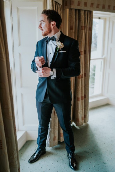 groom fixing his cufflinks looking out window