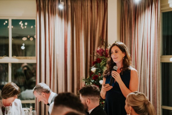 bridesmaid wearing black dress speaks into microphone giving speech