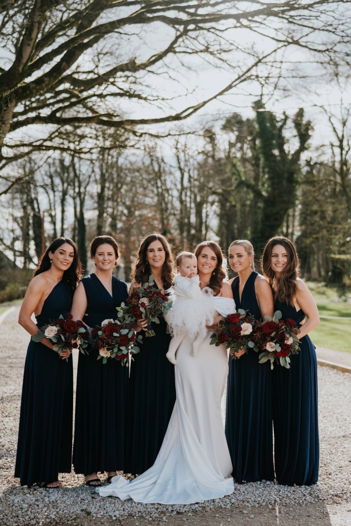 bride and bridesmaids pose on pathway to garden