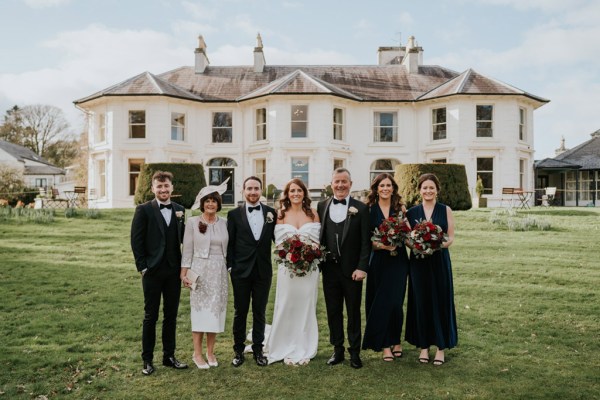 bride groom groomsmen and bridesmaids pose on the grass in front of wedding venue