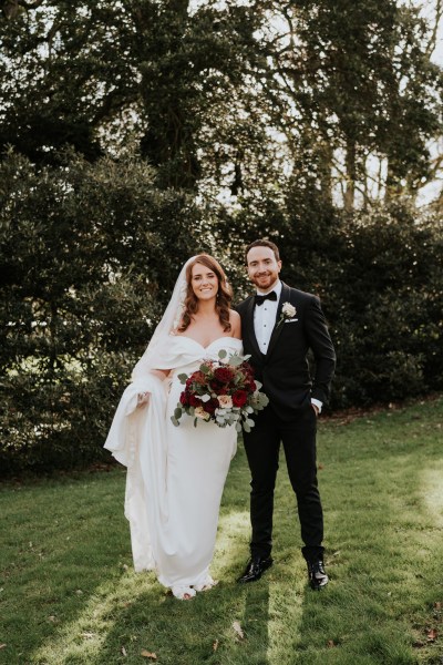 bride and groom pose standing on grass to garden