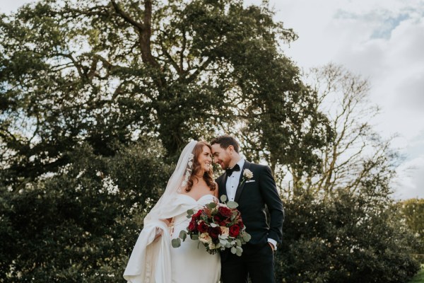 bride and groom pose standing on grass to garden touching foreheads