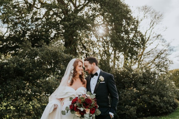 bride and groom pose standing on grass to garden touching foreheads