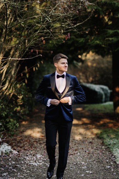 groom wearing suede blue jacket bowtie suit standing in garden