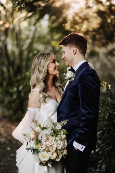 bride and groom look at each other in garden setting she holds bouquet