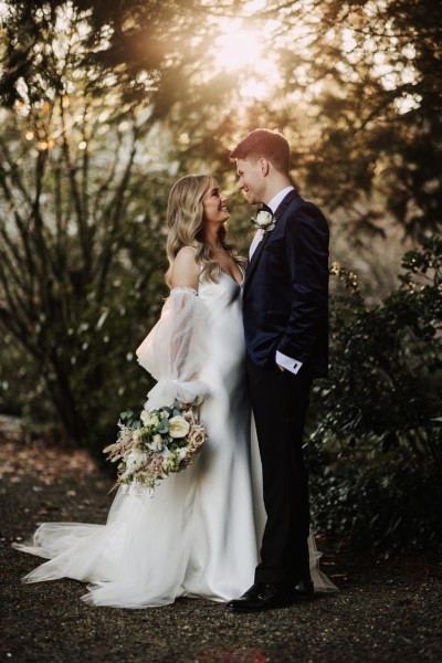 bride and groom look at each other in garden setting she holds bouquet