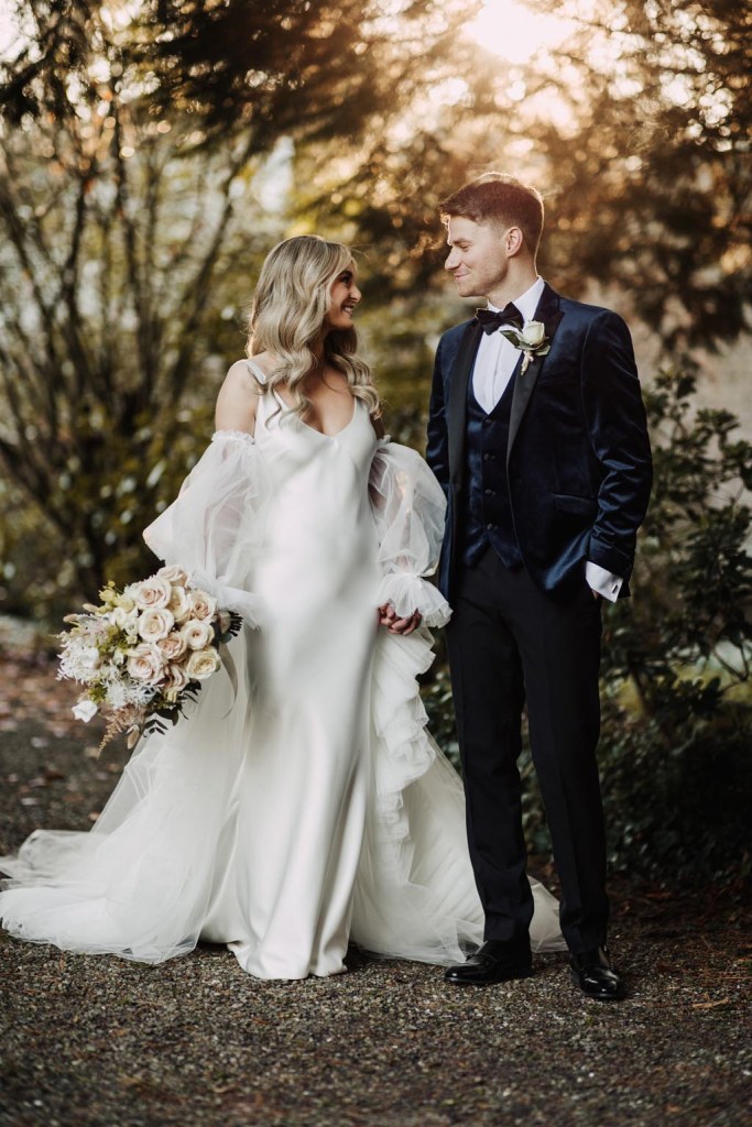 bride and groom look at each other in garden setting she holds bouquet