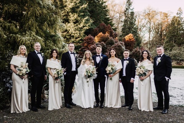 bride bridesmaids groom and groomsmen pose in a row outside in garden