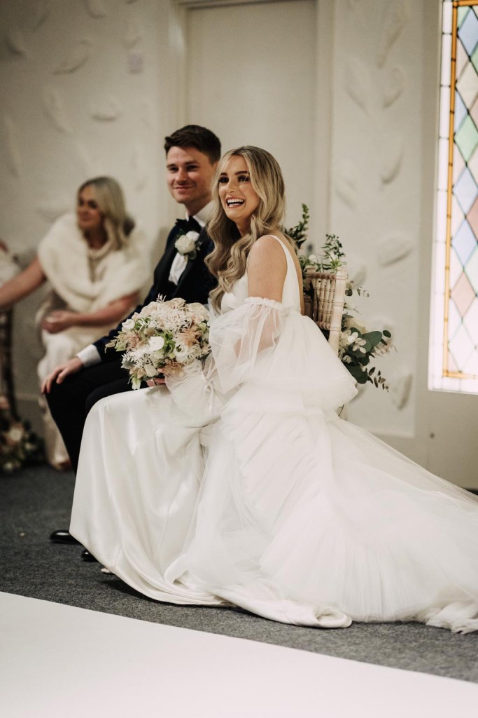 bride and groom bouquet on lap smiling at alter