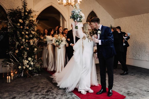 bride and groom stand on the red carpet bridesmaids in background bouquet in the air