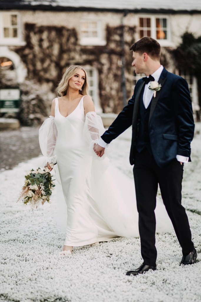 bride and groom standing on snow they walk she holds bouquet