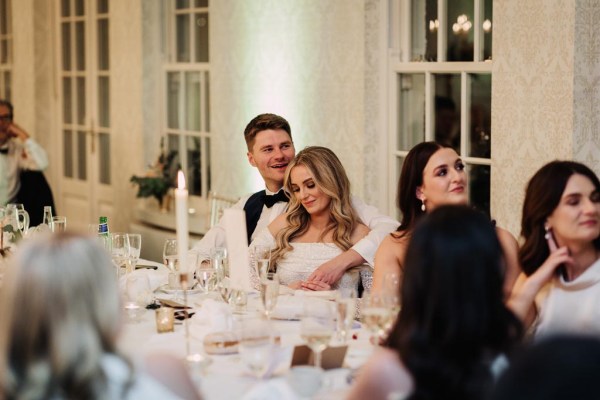 groom with arms wrapped around bride as they sit at table