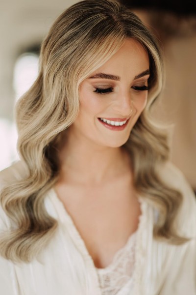 bride gets her makeup done wavy blonde hair smiling