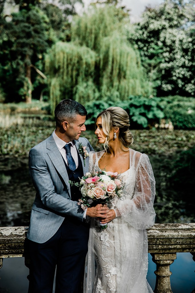 Bride and groom face each other green garden setting smiling bouquet in shot