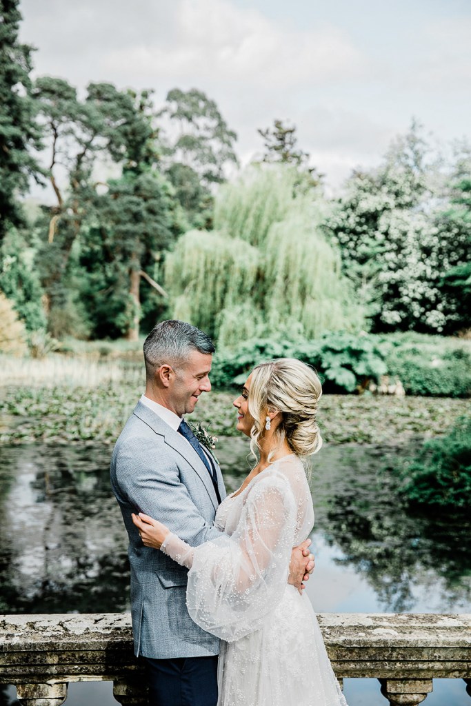 Bride and groom face each other green garden setting smiling