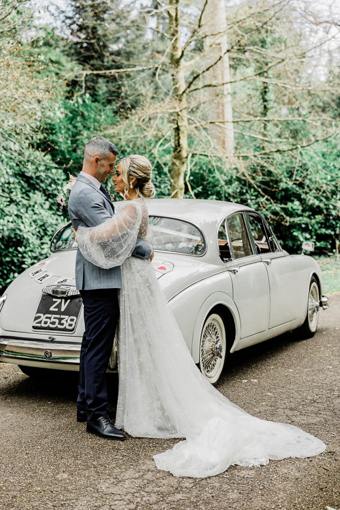 bride and groom hug closely beside wedding car