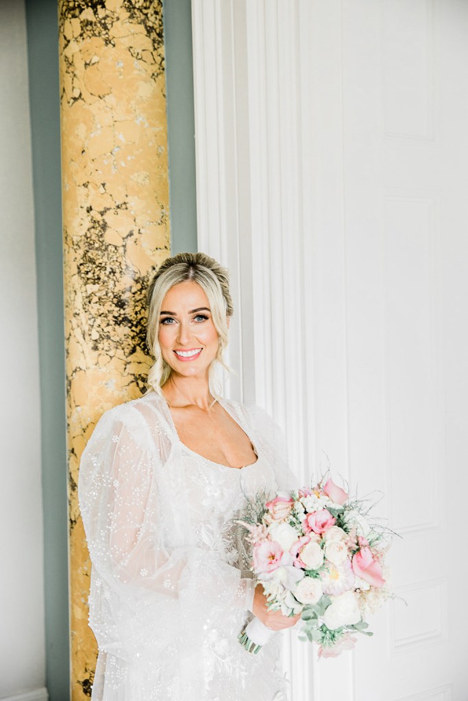 bride looks to her side holding bouquet flowers interior pillar room