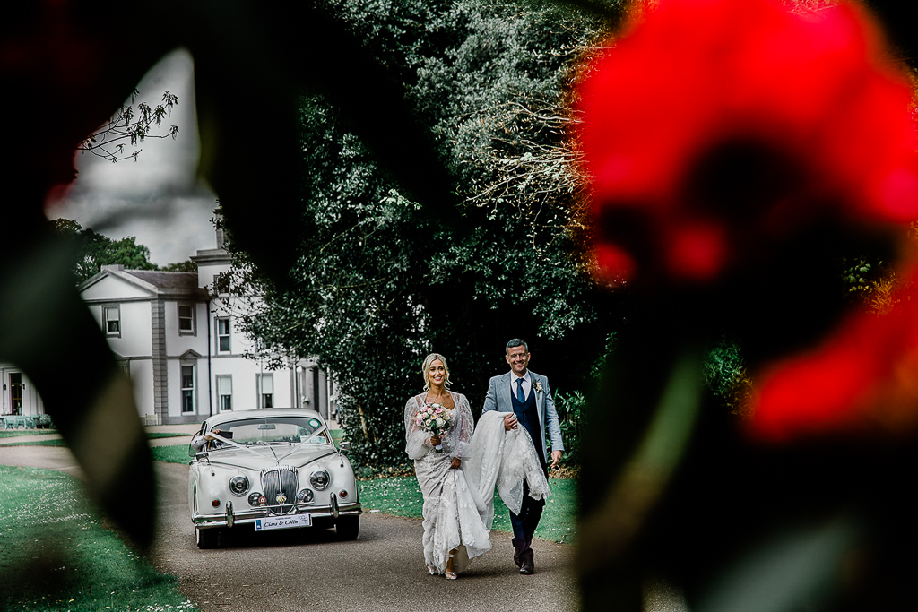 bride and groom walk the courtyard wedding car and venue behind them