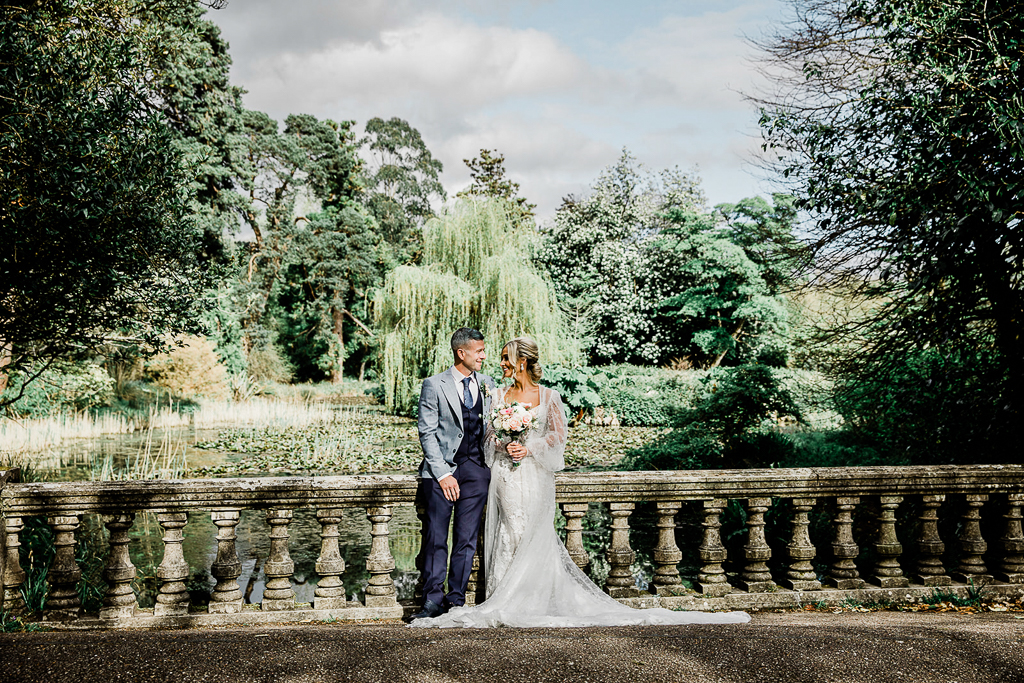 bride and groom stand at pillared balcony in front of garden forest setting