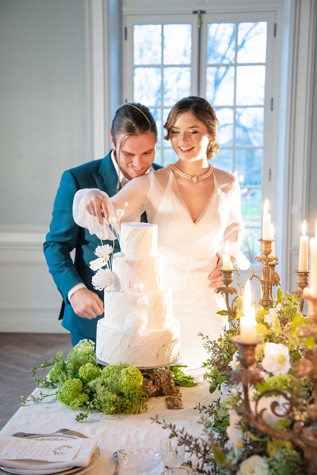 bride and groom cut the white wedding cake candles lit and flowers on table