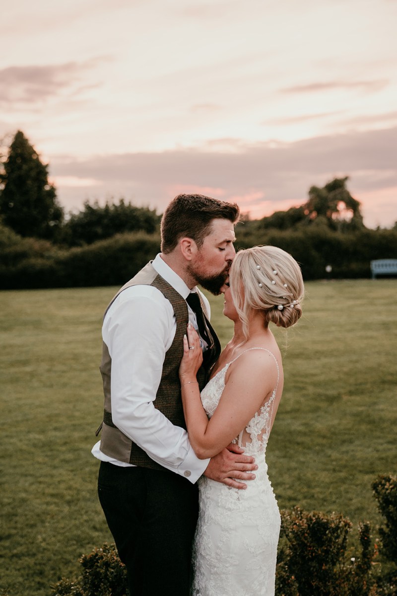 Groom kisses bride's forehead in their retreat to nature wedding